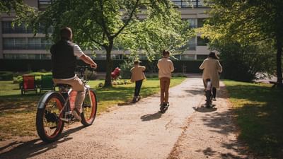 Family of four riding electric bikes on a path through a park with trees and a building.