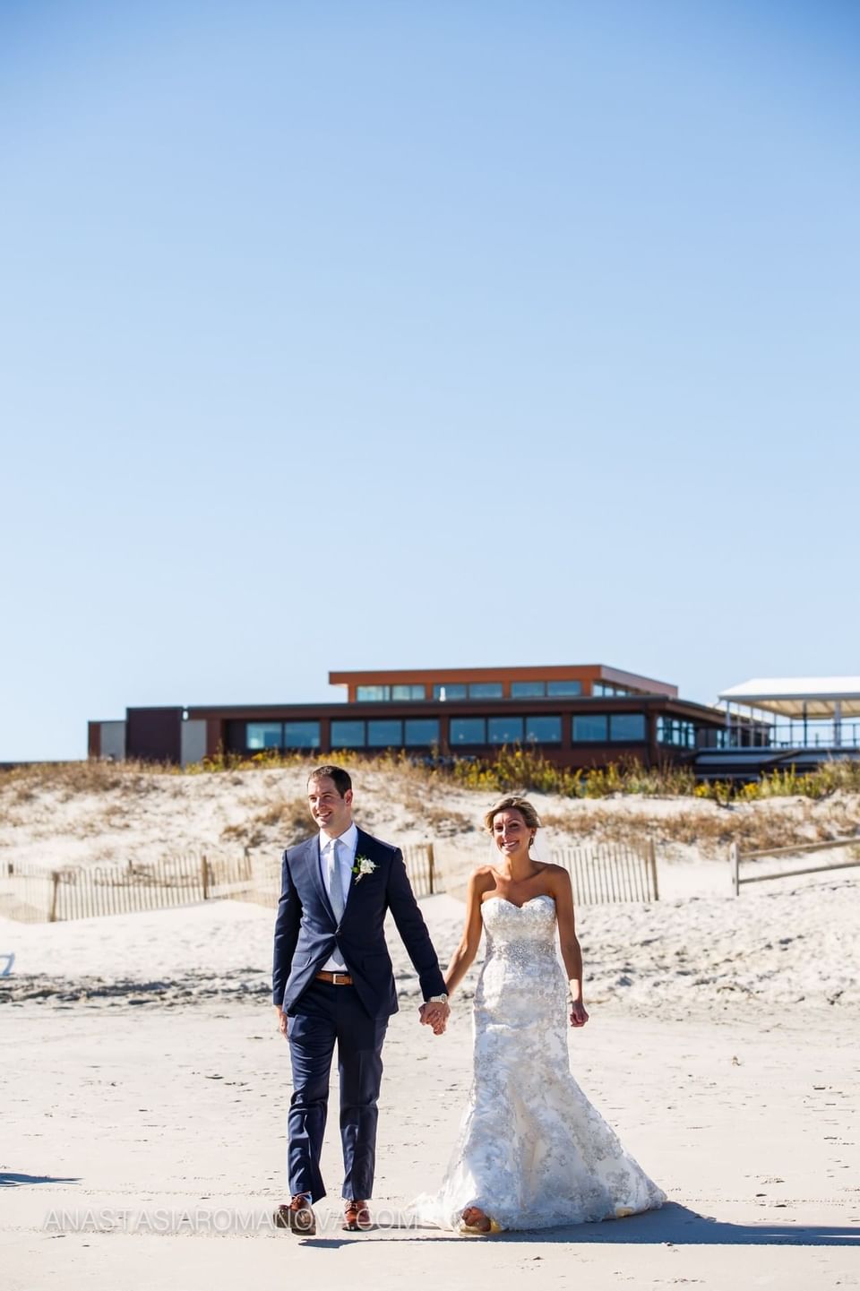 Newlyweds hold hands as they walk along the beach at our Avalon wedding venue