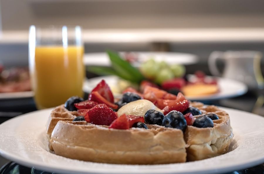 Waffles with berries by orange juice under soft light in In-Room Dining at Warwick Melrose Dallas
