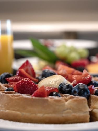 Waffles with berries by orange juice under soft light in In-Room Dining at Warwick Melrose Dallas