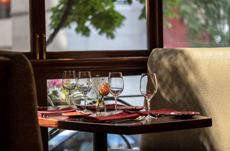 Set table by a large window featuring wine glasses and a single rose in Margaux Restaurant at Warwick Seattle
