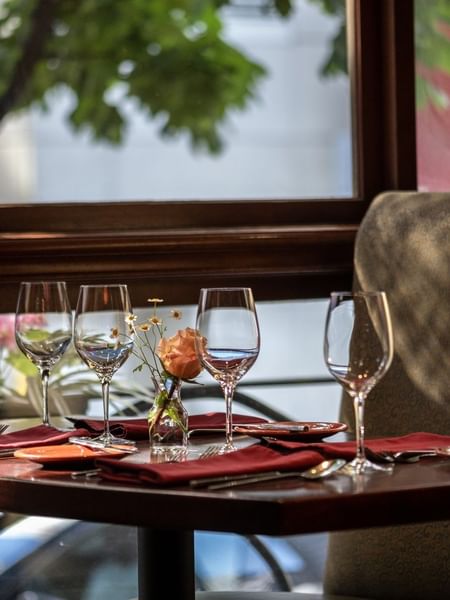Set table by a large window featuring wine glasses and a single rose in Margaux Restaurant at Warwick Seattle