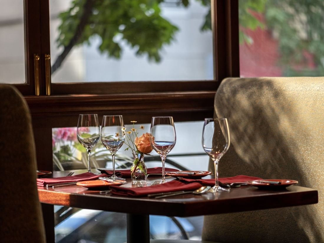 Set table by a large window featuring wine glasses and a single rose in Margaux Restaurant at Warwick Seattle