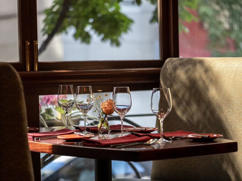 Set table by a large window featuring wine glasses and a single rose in Margaux Restaurant at Warwick Seattle