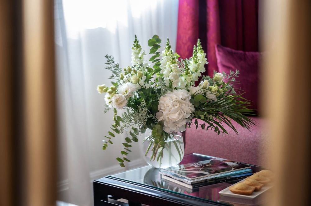 White flowers in a glass vase by magazines on a table in the Executive Room at Warwick Paris Champs Elysées