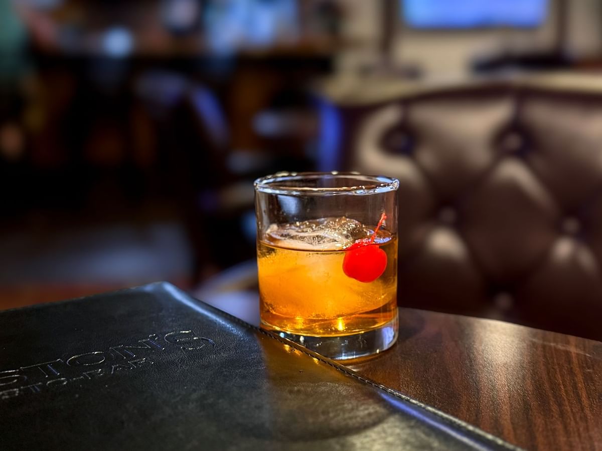 Glass of drink with a red cherry on a wooden table next to a menu.