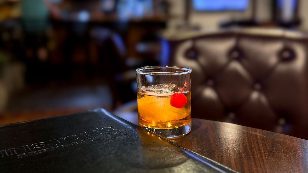 Glass of drink with a red cherry on a wooden table next to a menu.