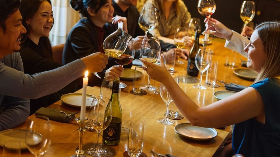 Group of friends toasting with wine glasses around a wooden table during a celebratory dinner gathering.
