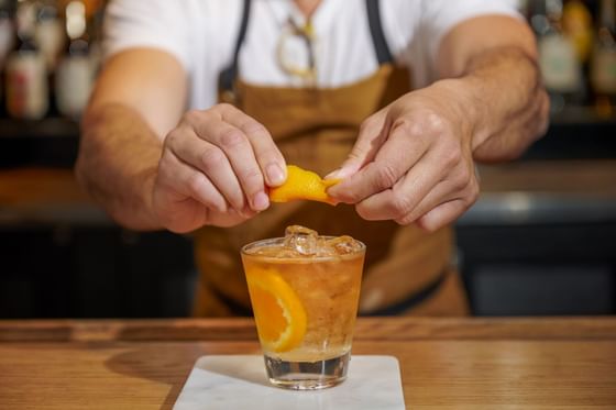 A bartender slicing an orange for a cocktail in Bar Luxe at Luxe Sunset Boulevard Hotel