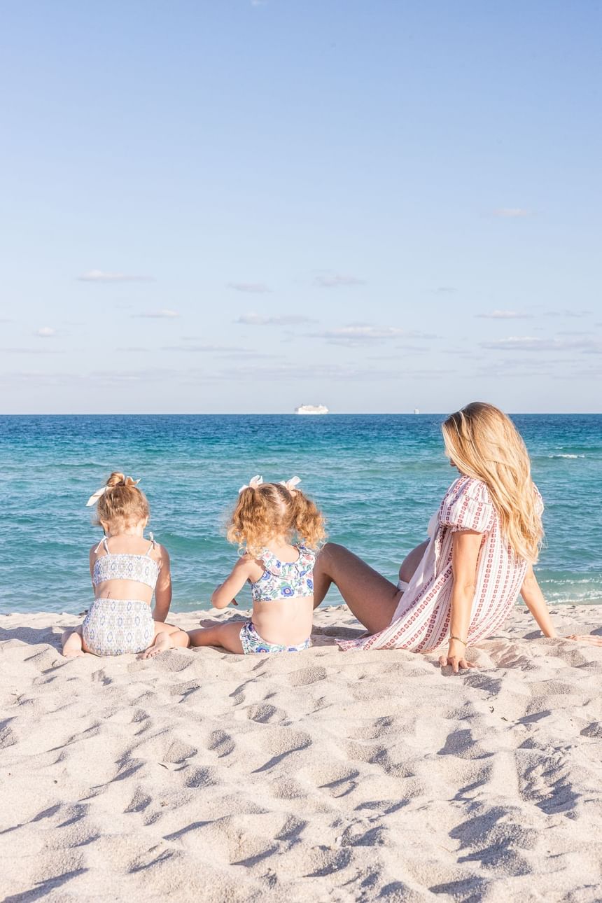 Mother & two children sitting on a sandy beach overlooking the sea near The Savoy Hotel & Beach Club