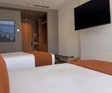 Wall-mounted television opposite modern double beds with orange runners in the guest room at Unika Hotels