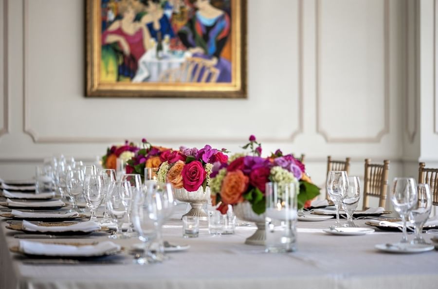 Floral centerpieces on a table by crystal glasses under a classic painting in The Bridewell Suite at Warwick Melrose Dallas