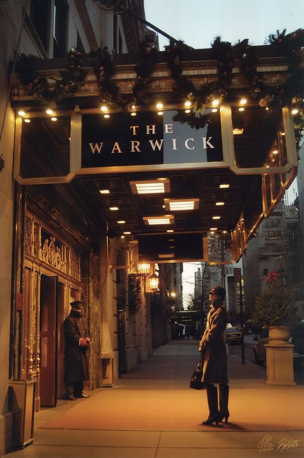 Woman stands in front of The Warwick hotel entrance with holiday decor at Warwick Corporate