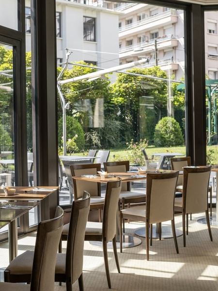 Roseraie Room with wooden tables, beige chairs, & large windows offering a lush garden view at Warwick Reine Astrid - Lyon