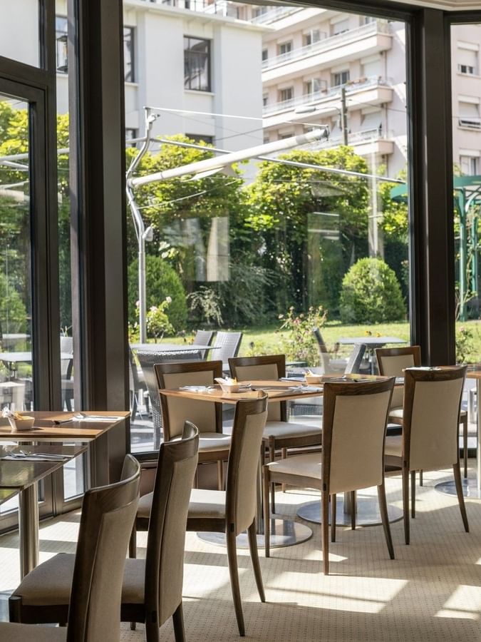 Roseraie Room with wooden tables, beige chairs, & large windows offering a lush garden view at Warwick Reine Astrid - Lyon