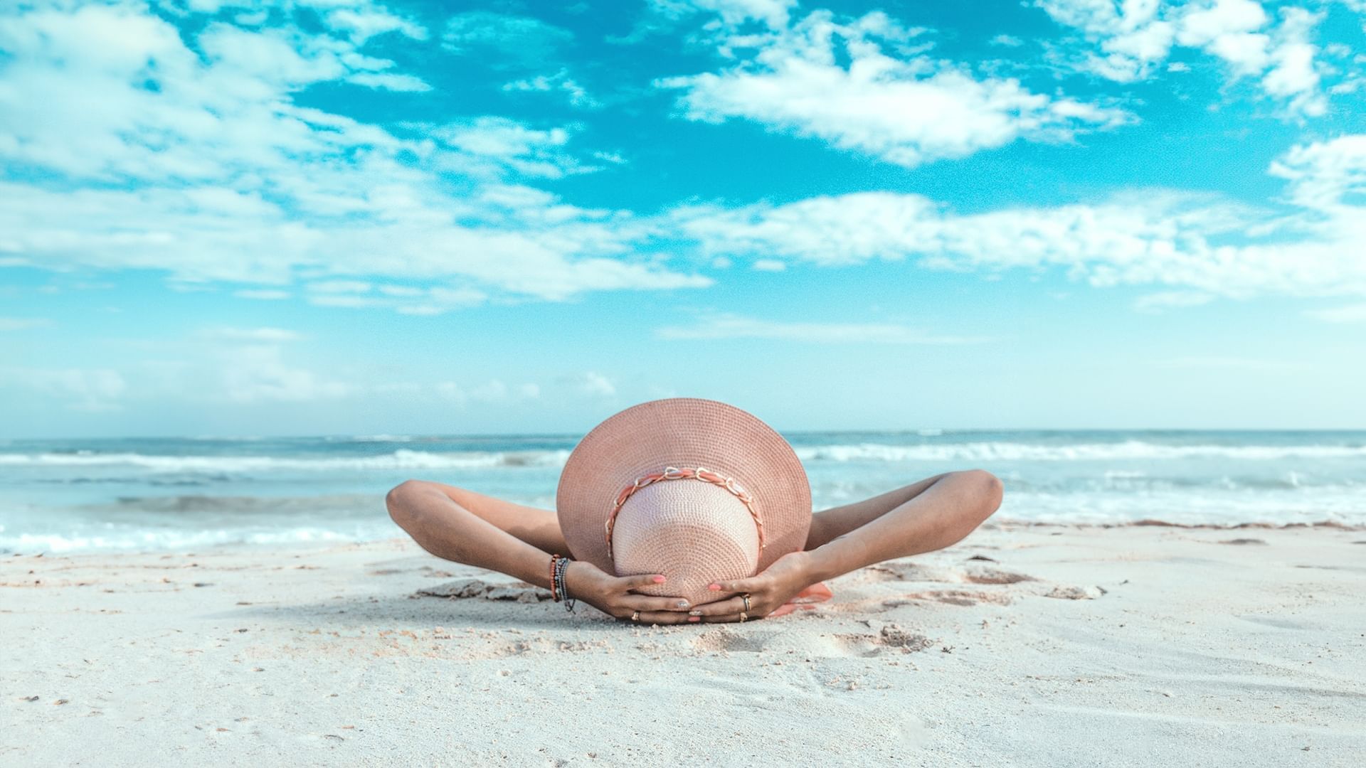 Person in a large straw hat lies on the beach overlooking ocean at Sunset Plaza Beach Resort