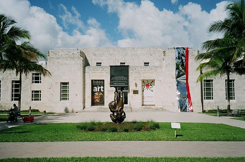 BASS -White building with a large sculpture in front and banners on the side, surrounded by palm trees.