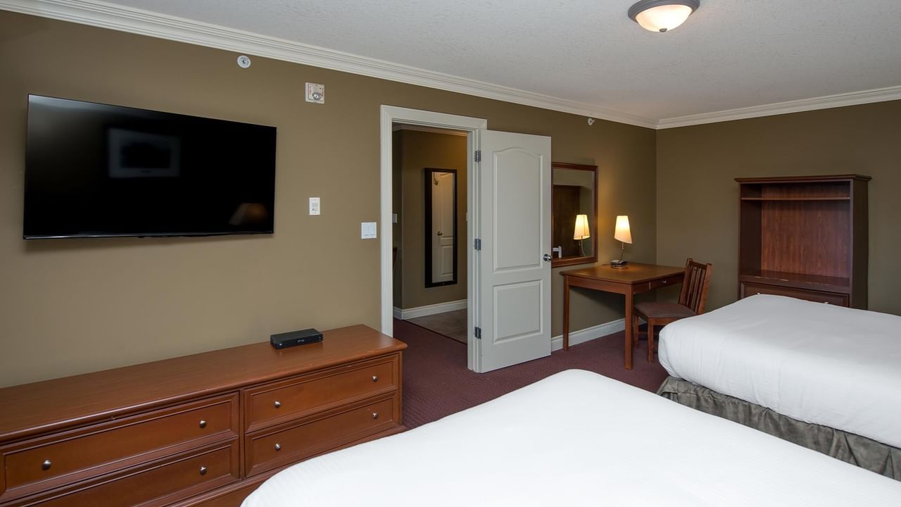 Spacious double room with two beds, wooden furniture, wall-mounted TV, and work desk at Coast Edson Hotel.