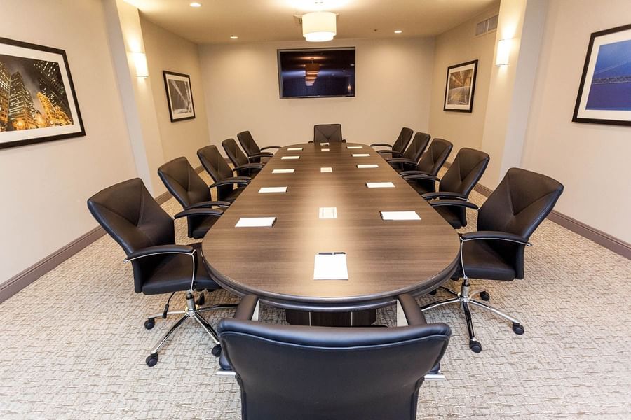 Black chairs by a long oval table under a flat-screen TV in Encore Room at Warwick San Francisco