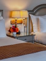 Two beds with patterned throws by a nightstand under warm twin wall lamps in Deluxe Double at Warwick Melrose Dallas