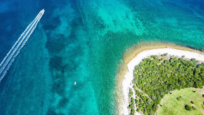 Aerial view of a boat near a tropical island with clear blue waters and greenery near Falkensteiner Hotels & Residences