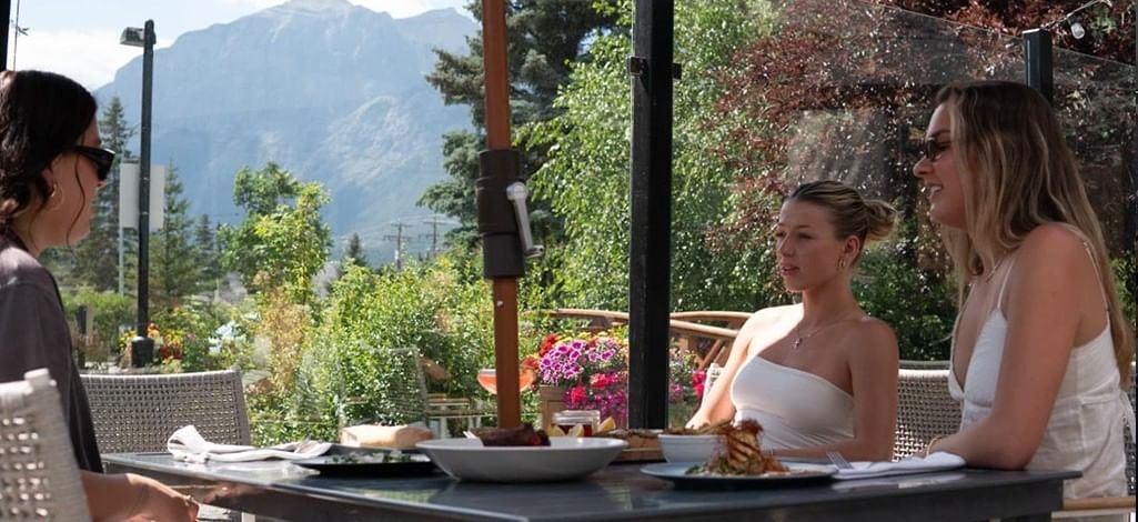 Three people enjoy lunch on the patio of a restaurant in Canmore in summer.