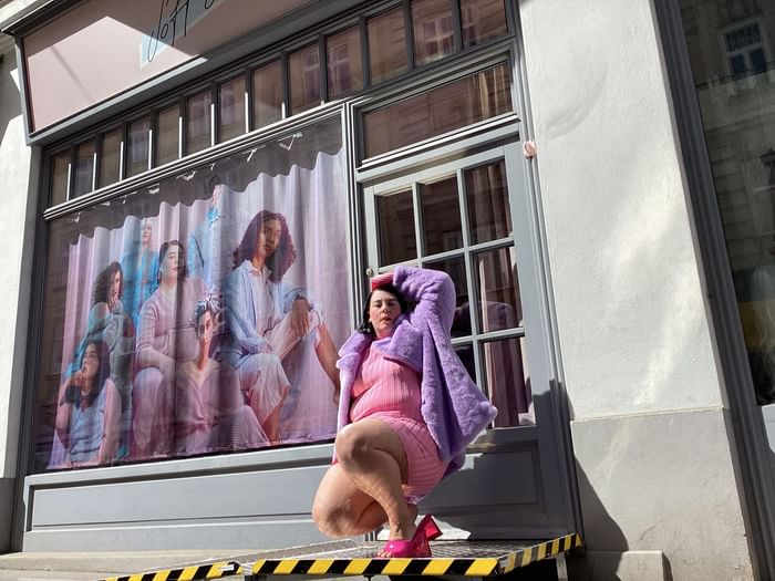 Ina Holub queer activist in pink and purple poses playfully on boutique steps with a colorful display at Hotel Motto Vienna