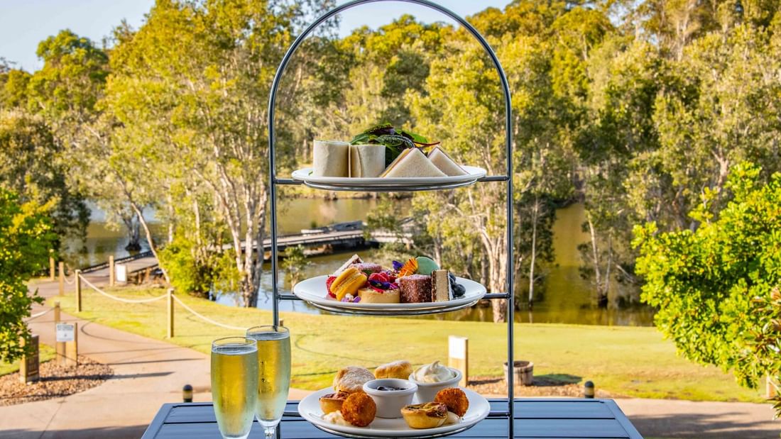Afternoon High Tea set on a table with a view of a lush park and river at Mercure Kooindah Waters
