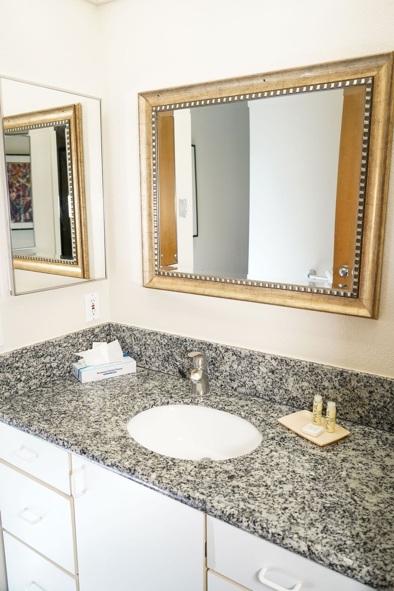A bathroom vanity with a granite countertop, white sink, and gold-framed mirror