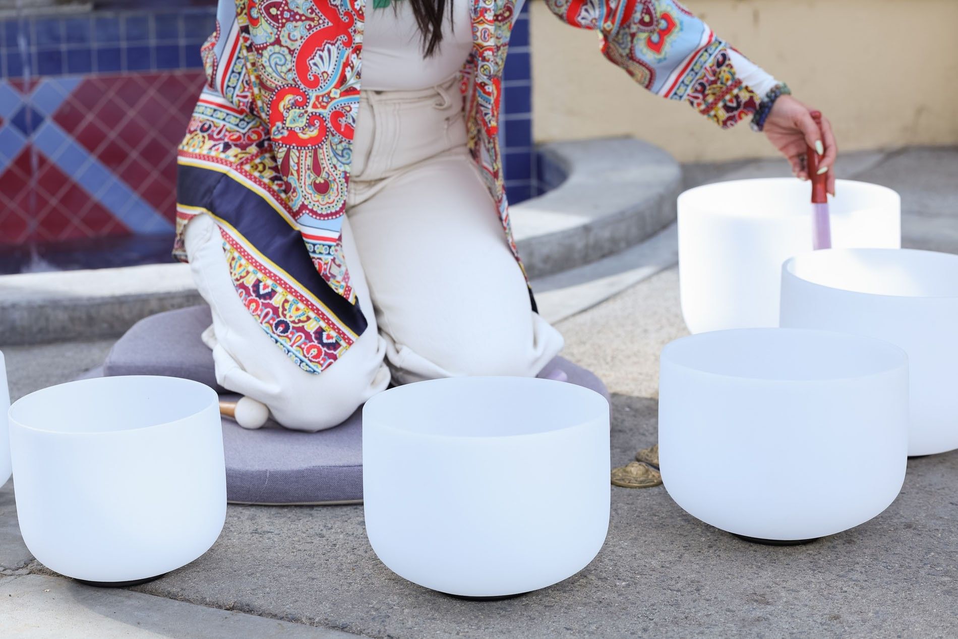 Person in a colorful paisley robe playing frosted white crystal singing bowls for a sound bath at Kelly's Spa