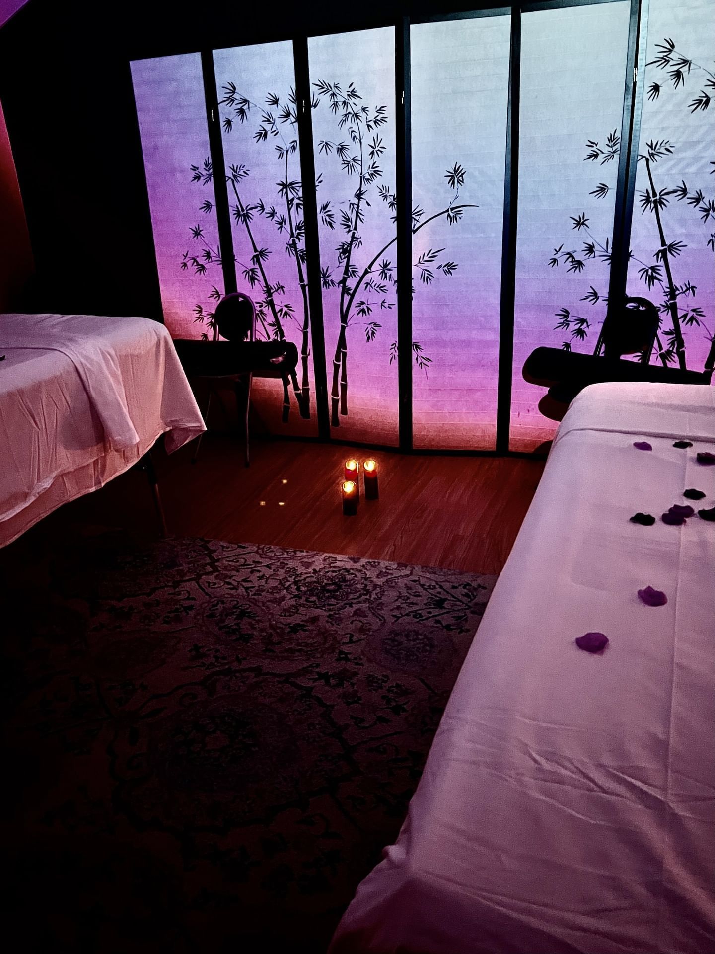 Spa room with two massage tables, soft lighting, a decorative bamboo screen, and candles in Cove Pocono Resorts