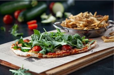 Pizza topped with arugula and tomatoes served in a restaurant at Acclaim Hotel Calgary