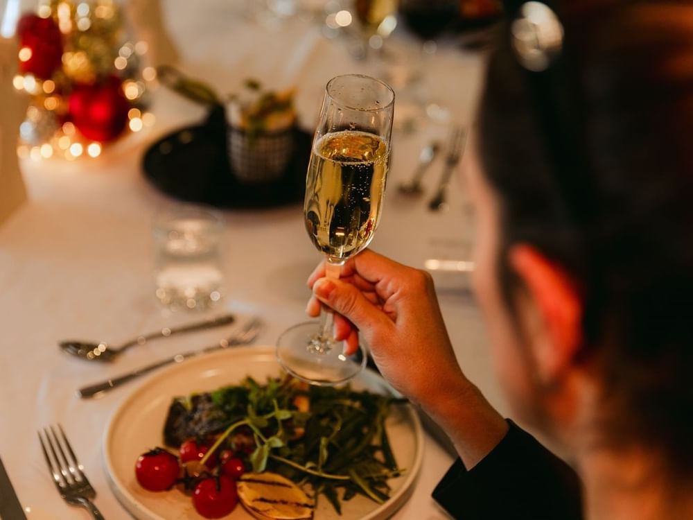 Person at a table with a champagne glass and plate of food.