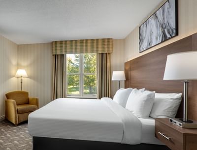 Bed with lamps & armchair near window in 1 Queen Bed Executive Wing Room at Spencer Hotel, best hotel suites London Ontario