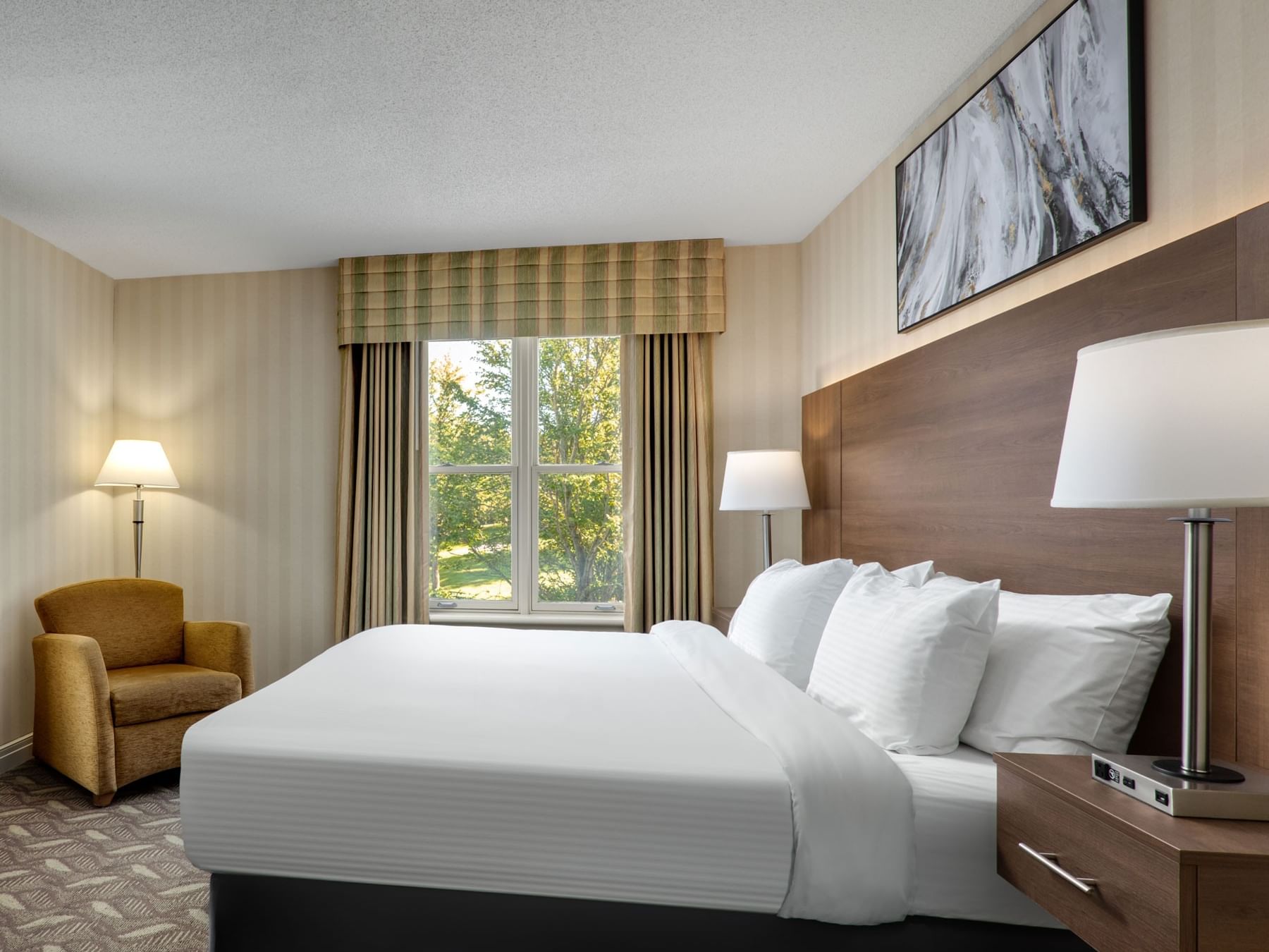 Bed with lamps & armchair near window in 1 Queen Bed Executive Wing Room at Spencer Hotel, best hotel suites London Ontario