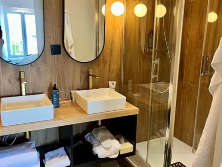 Deux lavabos, miroirs, douche en verre et serviettes dans la salle de bain de l'Hôtel Le Yachtman.