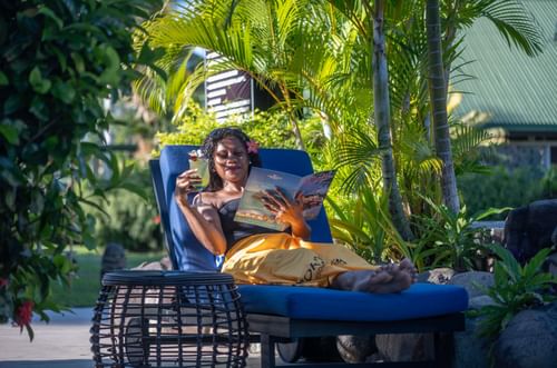 Guest enjoying a drink on a blue lounger by a wicker table near lush plants at TokaToka Resort Nadi Fiji