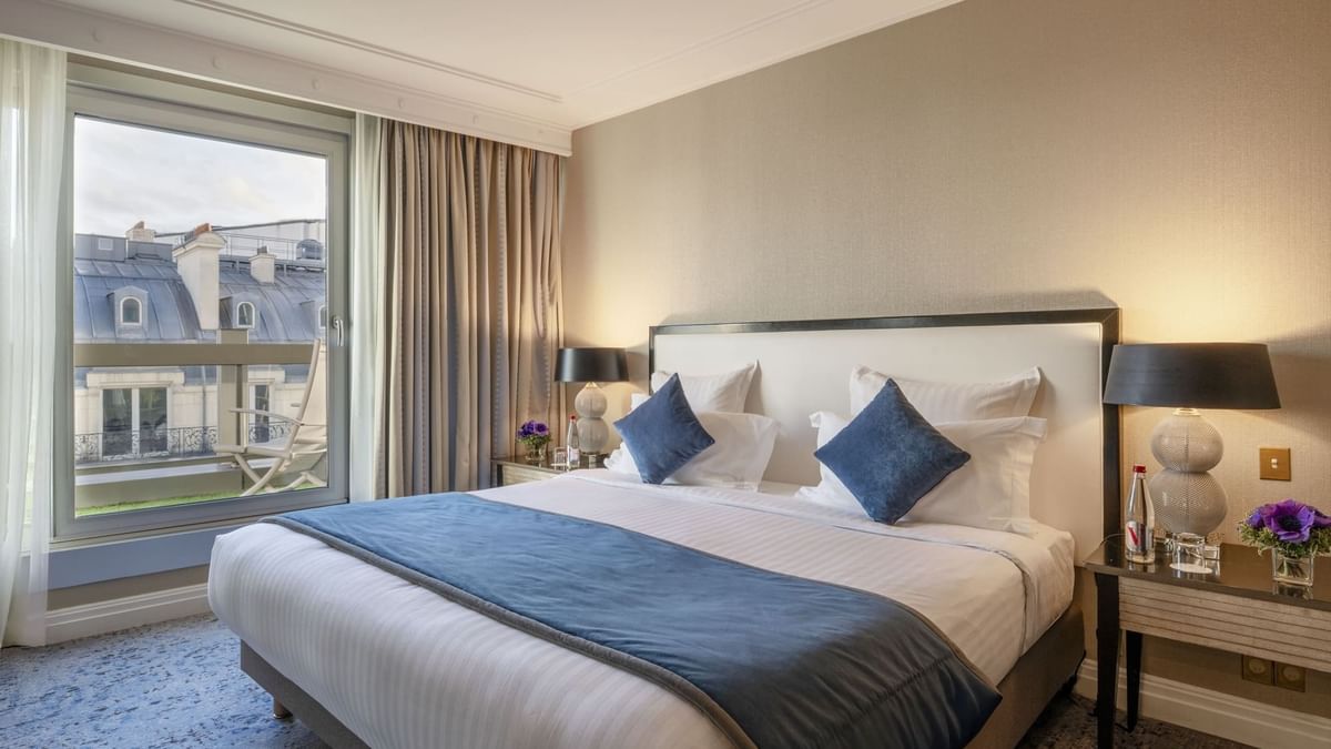 Un lit douillet, avec une parure de lit et des oreillers bleus et blancs, dans une suite de l'hôtel Warwick Champs-Élysées à Paris.