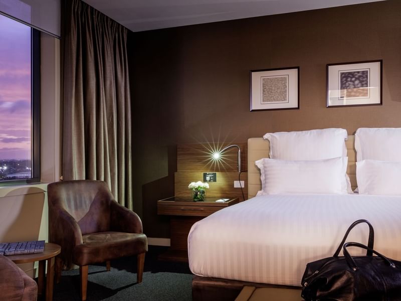 Bed with a couch by the windows and carpet floors in the Pullman Suite Bedroom at Pullman Sydney Olympic Park