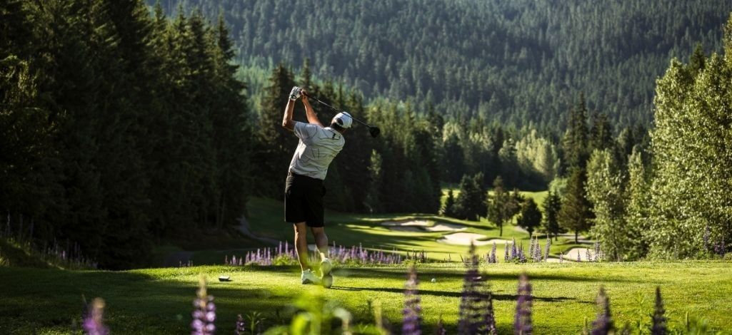 Golfer takes a swing on a forested fairway at Fairmont Chateau Whistler Golf Club.