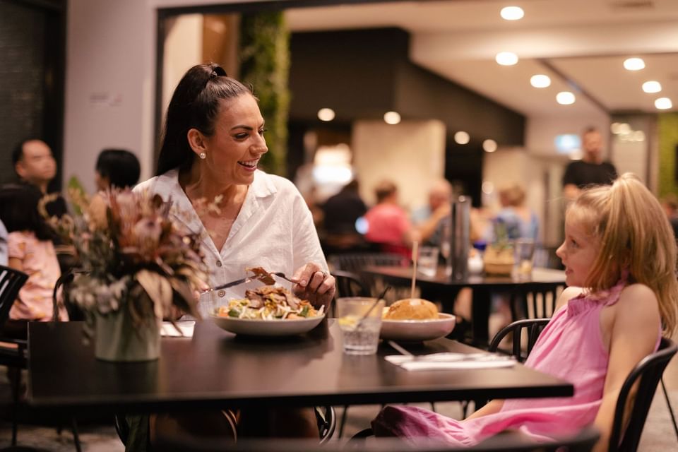 Lady and child dining in a busy restaurant with focus on a table with food at H on Mitchell