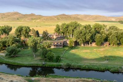 Aerial view of The Ranch at Ucross, showing buildings nestled among trees, a river, and rolling hills