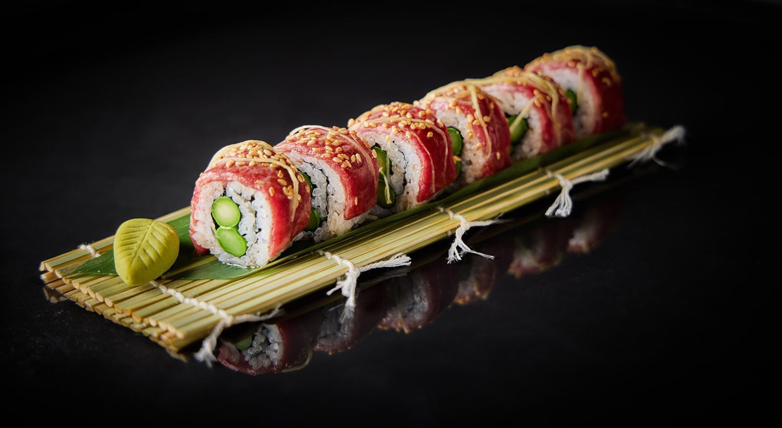 Exquisite sushi rolls with a delicate green filling and white sesame seeds, displayed on a bamboo mat at The Londoner Hotel