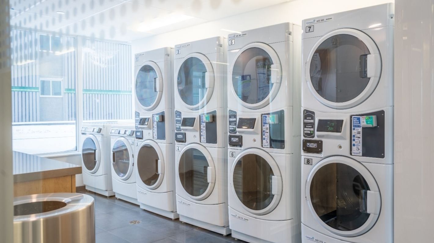 Row of high-efficiency stacked washers and dryers in a clean, well-lit on-site laundry room.
