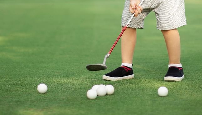 Primer plano de un niño golpeando pelotas de golf en Live Aqua Resorts
