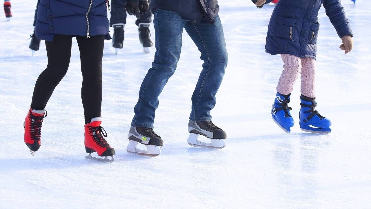 Three people ice skating on a frozen surface with other skaters in the background.