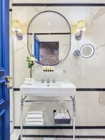 Salle de bains élégante avec une porte bleue, un lavabo blanc et des murs en marbre dans une chambre Deluxe de l'Hôtel Westminster à Paris.