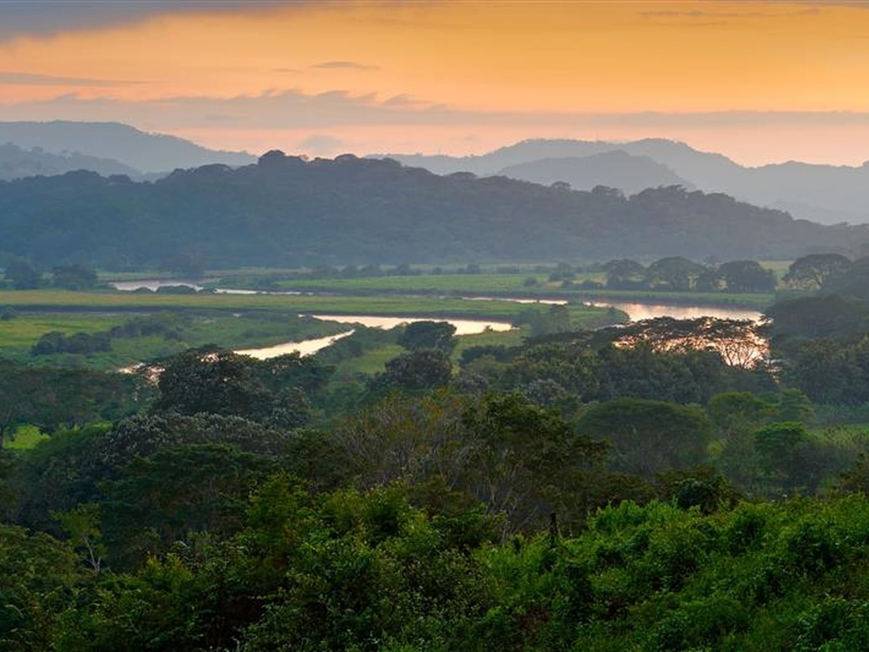 Sunset over Carara National Park, with winding trees reflecting on hazy hills near Santa Lucia Jungle Hacienda