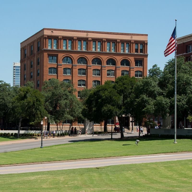 The historic red-brick building of the Sixth Floor Museum surrounded by trees near Warwick Melrose Dallas