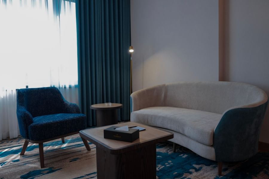 Modern lounge with blue couch and chair near a window at Warwick Hotel & Spa - Jeddah.